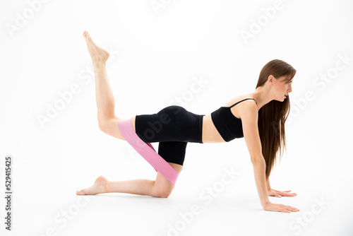 Sporty beautiful girl in sportswear is training with an expander on the floor on a white background