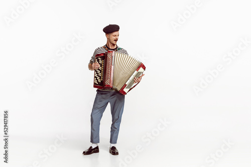 Portrait of young man playing accordion, posing isolated over white studio background. Countryside music