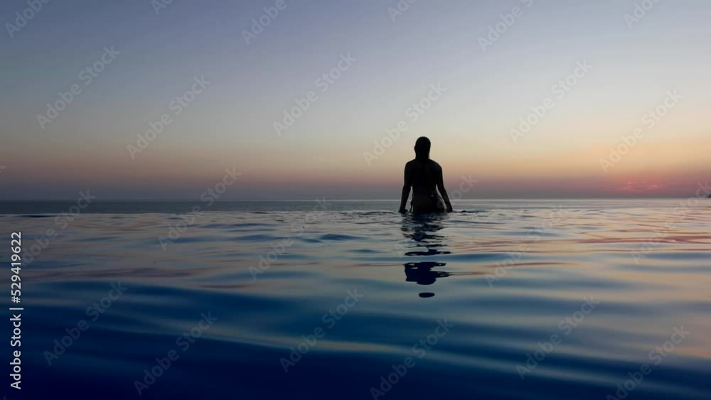 Beautiful woman relax in infinity swimming pool at luxury hotel spa enjoy golden sunset view of ocean mediterranean travel holiday resort. Female silhouette High quality slow motion 4k raw video Beautiful woman relax in infinity swimming pool at luxury hotel spa enjoy golden sunset view of ocean mediterranean travel holiday resort. Female silhouette High quality slow motion 4k raw video