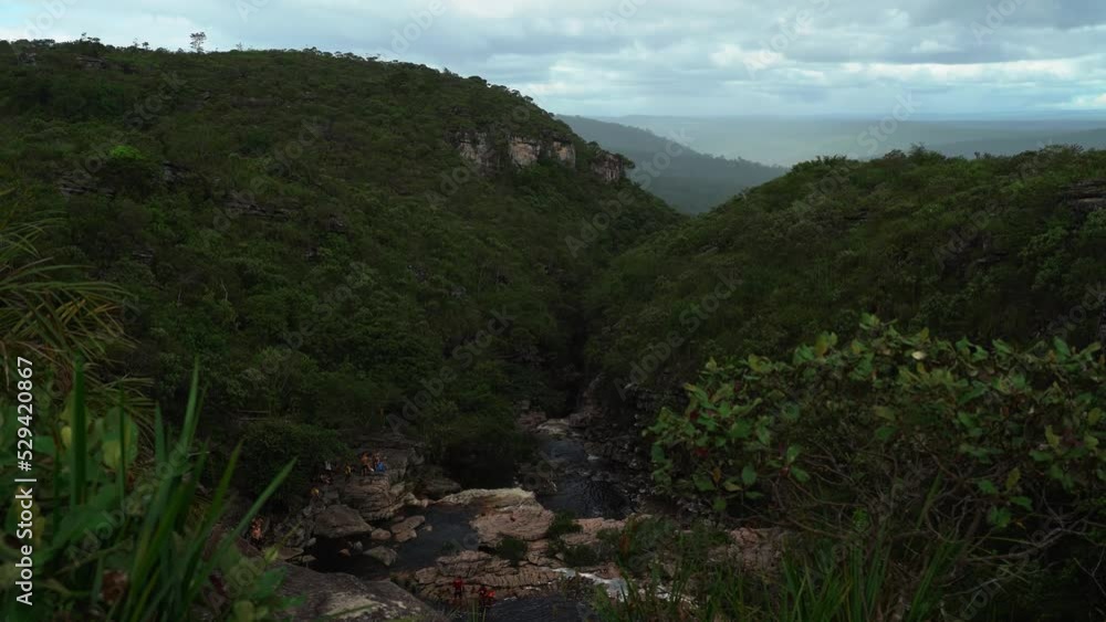 Handheld 4K shot revealing the Devil's Pit from the trail above in the Chapada Diamantina National Park in Northeastern Brazil on a rainy overcast day with people below near the water.