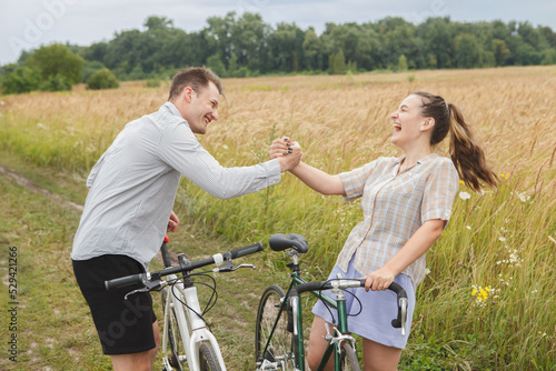 The happy couple cycling near the field. Cyclists man and a woman with bicycles go near the fields in summer.
