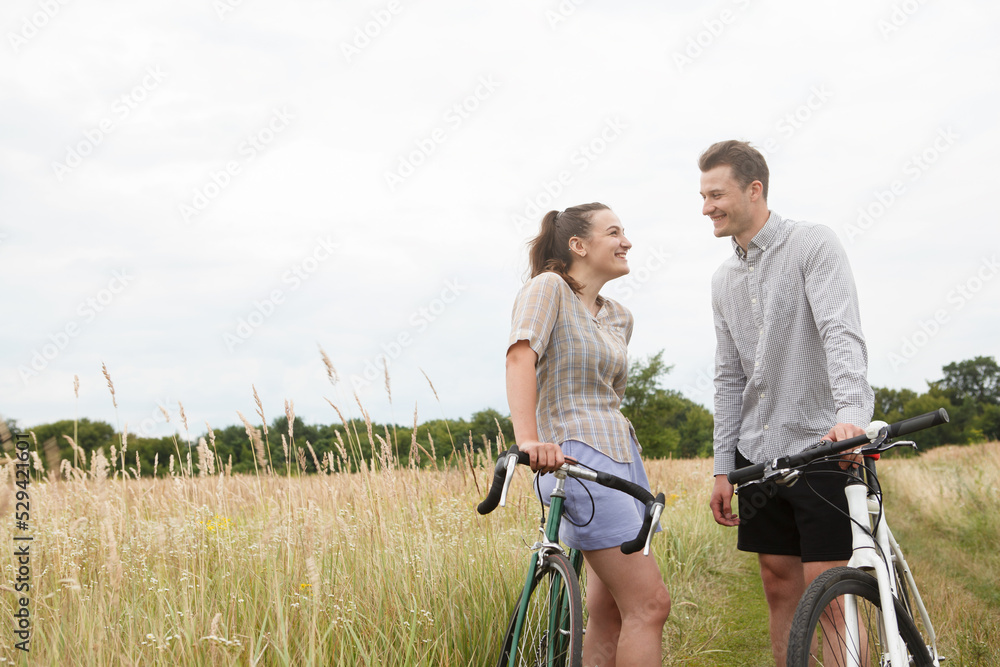Obraz premium The happy couple cycling near the field. Cyclists man and a woman with bicycles go near the fields in summer.