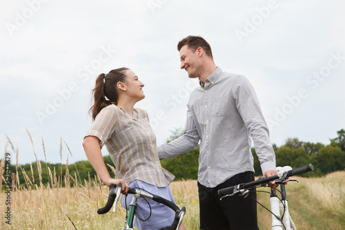 The happy couple cycling near the field. Cyclists man and a woman with bicycles go near the fields in summer.