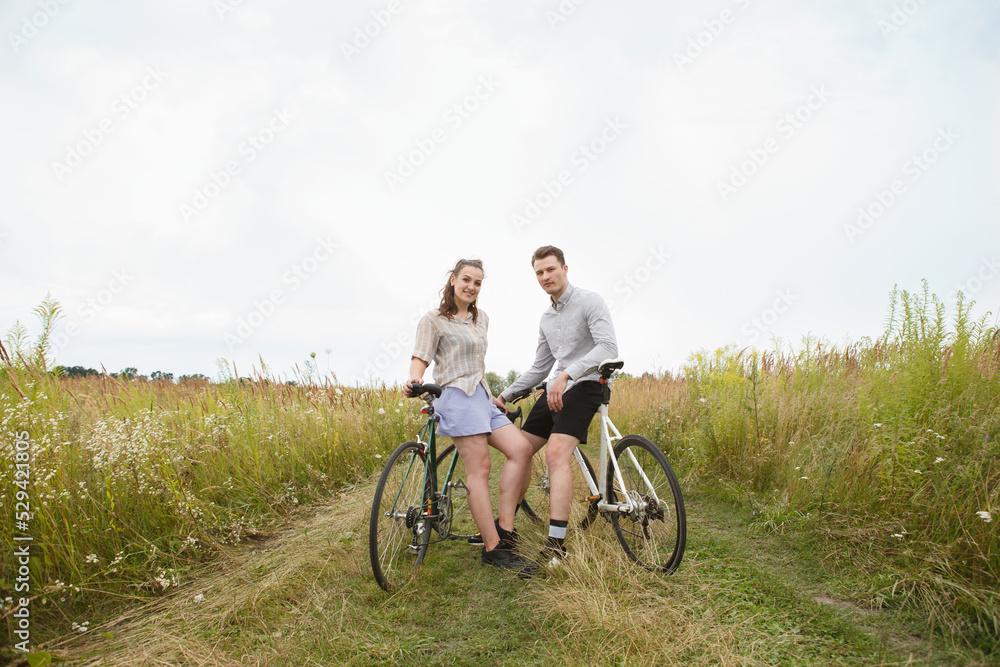The happy couple cycling near the field. Cyclists man and a woman with bicycles go near the fields  in summer.