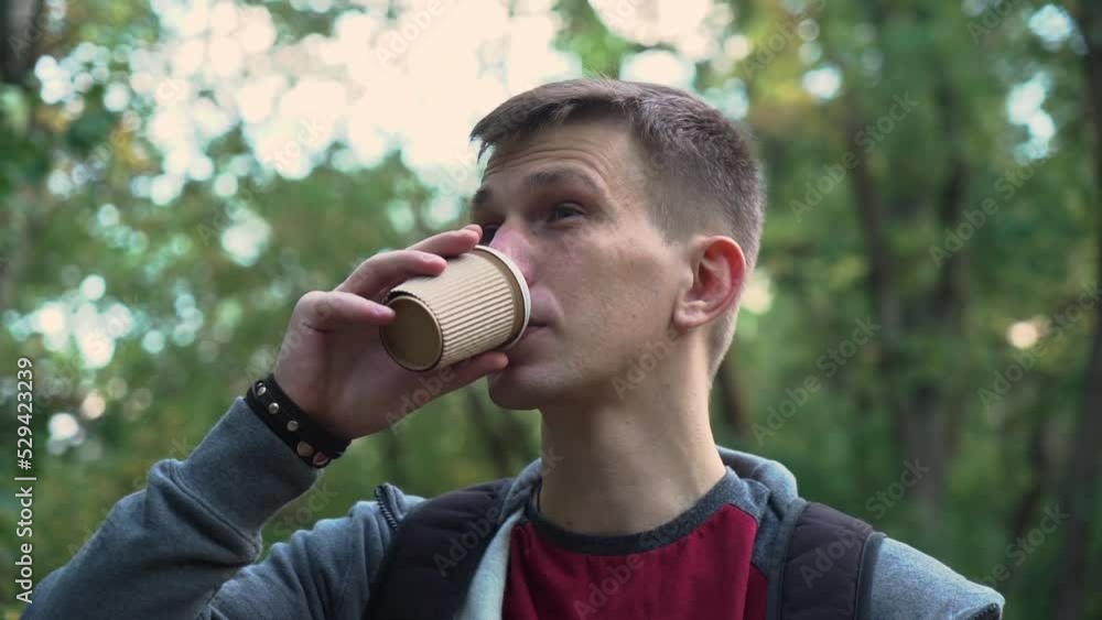 young guy is walking in the park with a cup of coffee. sunset. close-up young guy is walking in the park with a cup of coffee. sunset. close-up