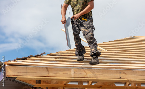 Workers install metal roofing on the wooden roof of a house.