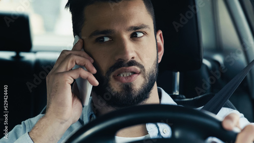 thoughtful bearded man driving auto during conversation on smartphone.