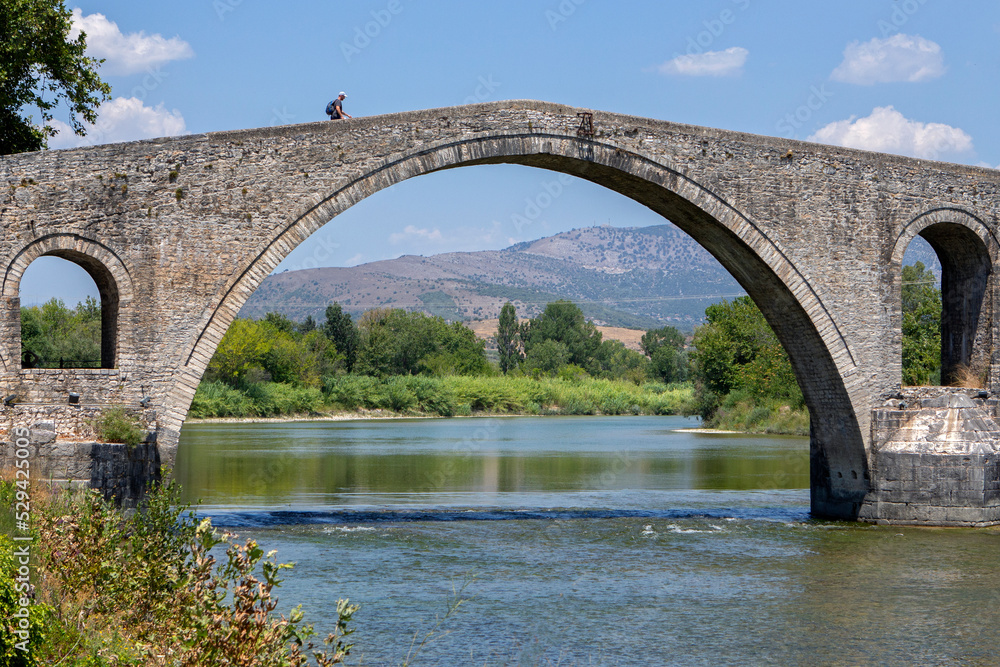 Fototapeta premium The Bridge of Arta. A stone bridge that crosses the Arachthos river in the west of the city of Arta in Greece. Sunny summer day with blue sky