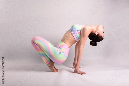 A beautiful slender gymnast in a stretch in a tracksuit does sports or yoga in the studio flexibly bending her torso and body in the studio on a white background