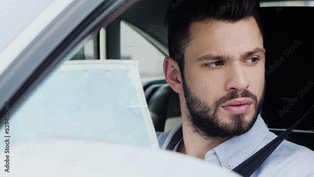 Fototapeta premium young bearded man looking away while sitting in car with map.