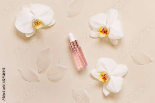 Pink Dropper Bottle near white orchid flowers on light beige top view. Skincare beauty product