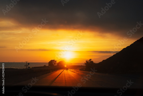 Stunning golden orange sunset on highway 101 California with few cars ocean and mountains. Road trip west coast USA
