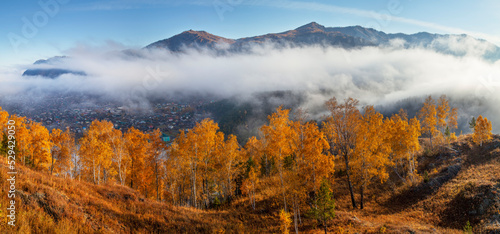 Panoramic autumn view, Altai nature. Fog above the mountain valley, the village below.