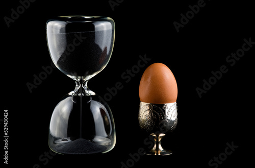 Hourglass Timer With Egg in Eggcup on a Dark Table Cloth