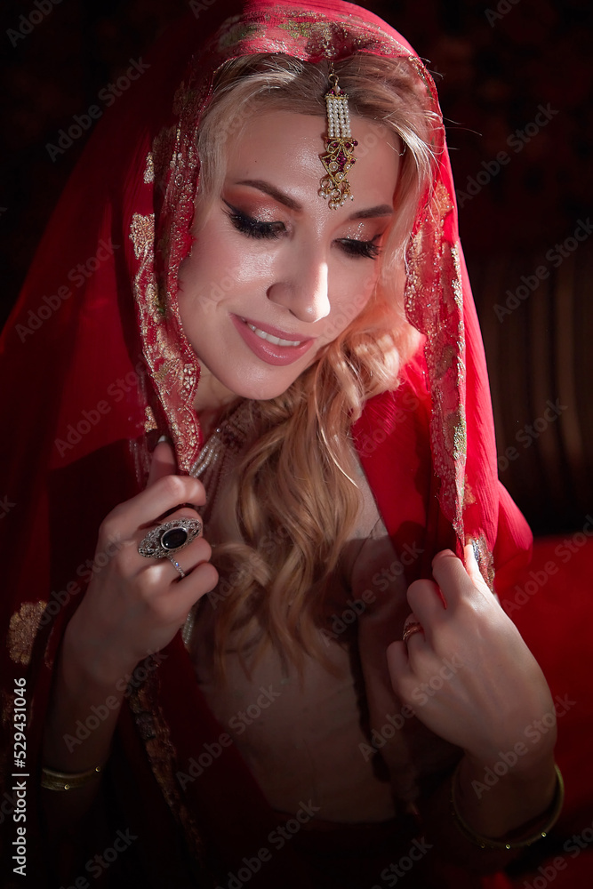 A beautiful European girl looking like an Arab woman in a red room in a harem. Photo shoot of an oriental style odalisque. A model poses in a sari as an indian woman in india A beautiful European girl looking like an Arab woman in a red room in a harem. Photo shoot of an oriental style odalisque. A model poses in a sari as an indian woman in india