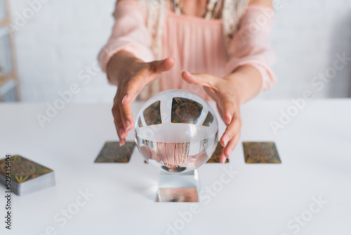 KYIV, UKRAINE - JUNE 29, 2022: selective focus of crystal ball near cropped fortune teller on blurred background. photo