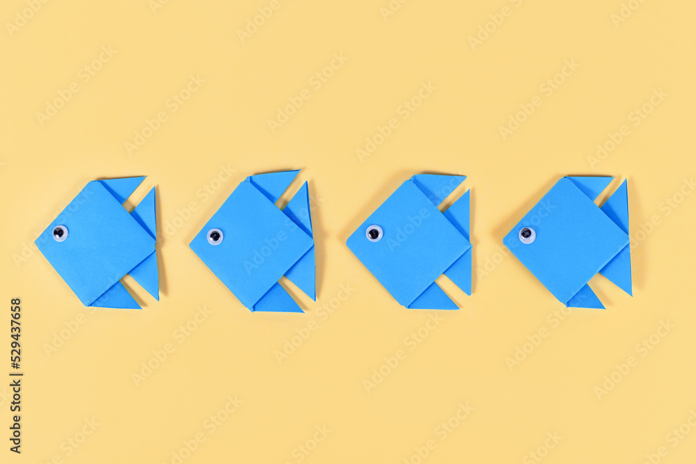 Blue origami paper fish swimming in a row on yellow background Blue origami paper fish swimming in a row on yellow background