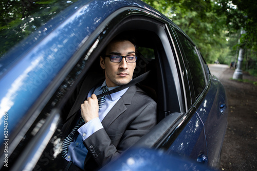 Handsome businessman in black suit fastening belt driving in luxury car © Vitaliy