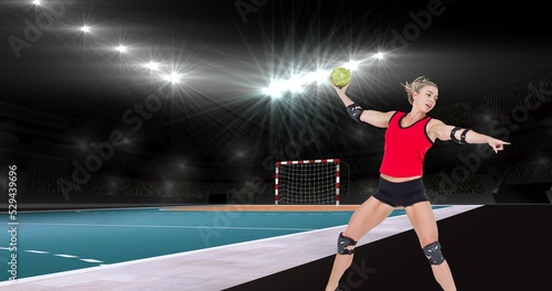 Focused caucasian female handball player pointing while throwing ball at illuminated stadium