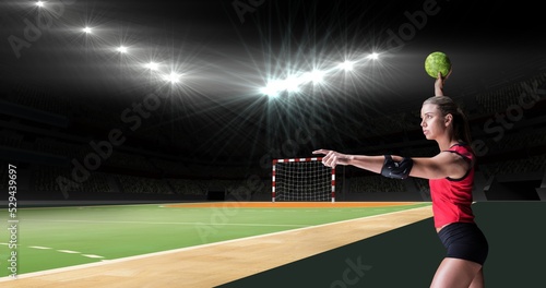 Caucasian female handball player pointing away while holding ball at illuminated stadium