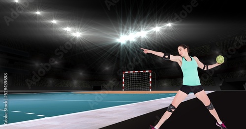 Female caucasian handball player pointing away while holding ball at illuminated stadium