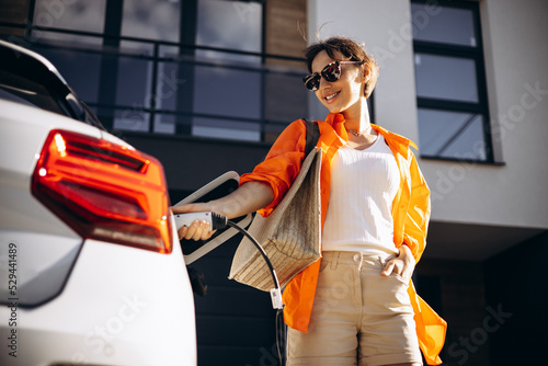 Bild auf Leinwand Woman charging electric car by her house