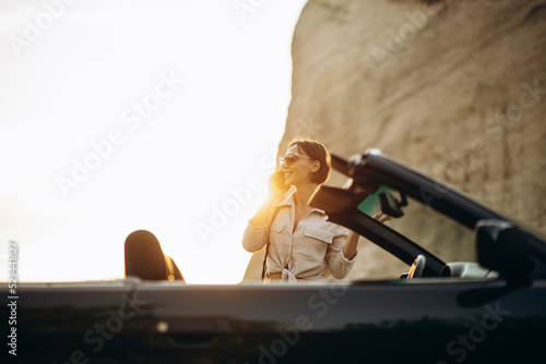 Young woman using phone and standing by her car