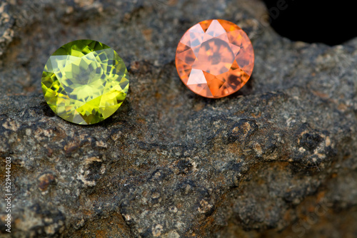 Green peridot chrysolite and orange color natural zircon round faceted loose transparent gemstones settings on raw uneven 
 stone surface dark background. Gemelogy mineralogy theme. photo