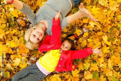 mother and daughter lying on the leaves at the autumn park.