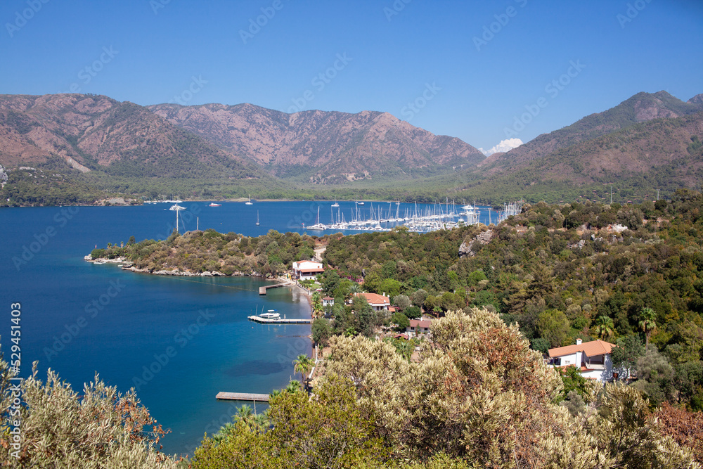 Landscape view of sea bay with marina in Turkey from above. Seascape with blue sea water and mountains with green trees.