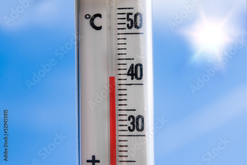 a weather thermometer reaching high temperatures over 40 degrees during heat wave in europe on a very hot day with the sun and a blue sky and sun reflections in the background america asia china world