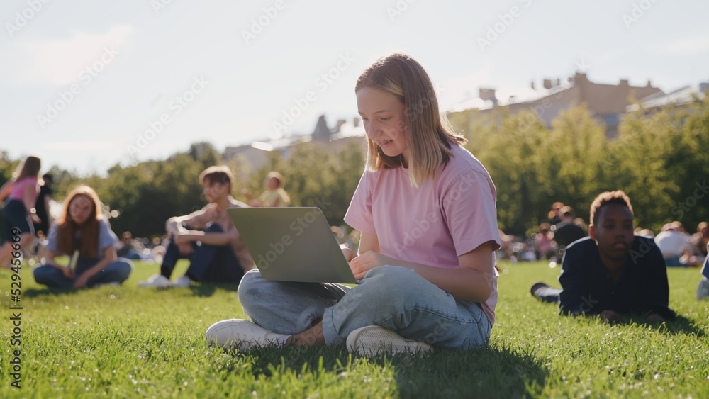 Schoolgirl using laptop while sitting on green grass of campus lawn. Schoolgirl using laptop while sitting on green grass of campus lawn.
