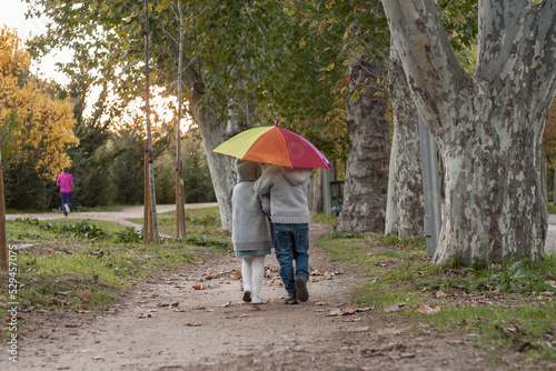 dos hermanos caminando por un bosque en otoño con un paraguas aco iris photo