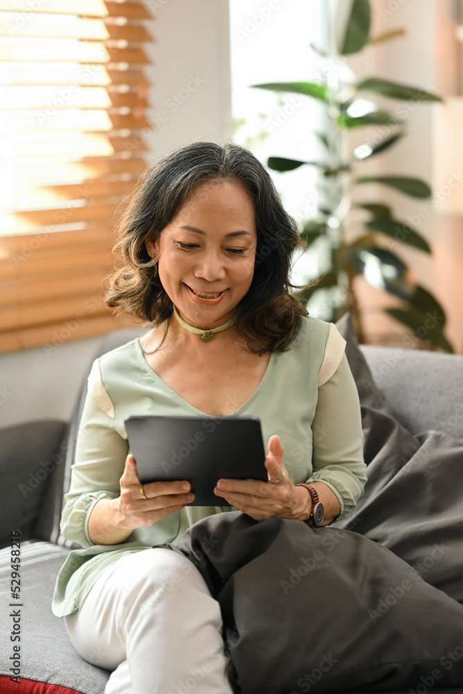 Positive middle aged woman relaxing on couch and enjoy surfing internet on digital tablet Positive middle aged woman relaxing on couch and enjoy surfing internet on digital tablet