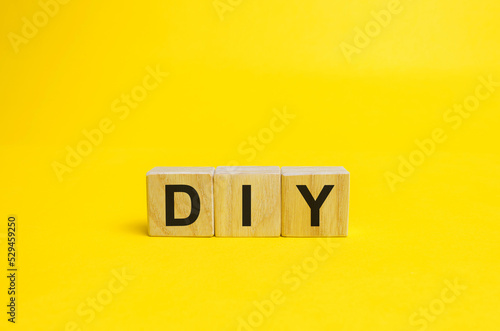 Wooden blocks with the word DIY — Do It Yourself concept. The method of self-creation of things without the help of professionals. yellow background