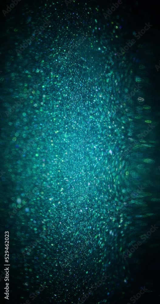 Glitter texture background. Blur particles. Light flare. Defocused fluorescent blue green color sparkles motion on dark abstract overlay. Vertical video. Shot on RED Cinema camera. Glitter texture background. Blur particles. Light flare. Defocused fluorescent blue green color sparkles motion on dark abstract overlay. Vertical video. Shot on RED Cinema camera.