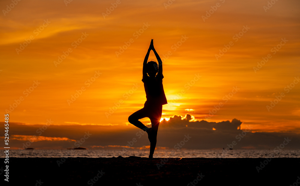 Silhouette of young girl practicing yoga on the beach at beautiful sunset sky in evening.
