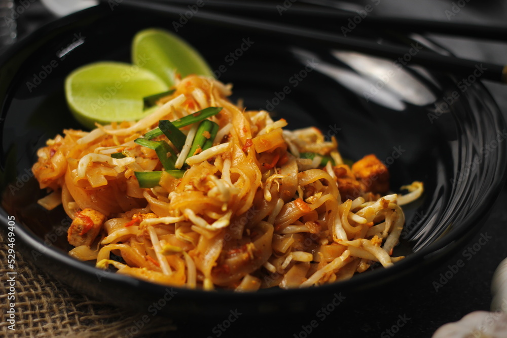 Pad Thai or Fried noodle Thai style, Thai style served with lime and seasonings. In a black palette, the visual style is dark tones. Pad Thai or Fried noodle Thai style, Thai style served with lime and seasonings. In a black palette, the visual style is dark tones.