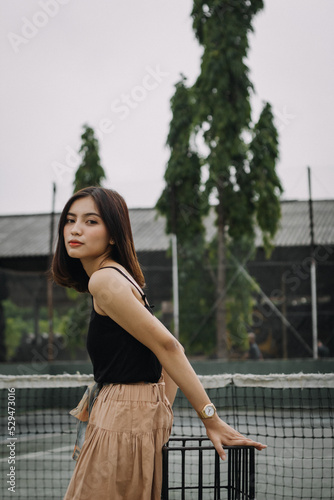 Beautiful female model, wearing a black tanktop, posing and stylish in the middle of a tennis court in the afternoon. © ajiilhampratama
