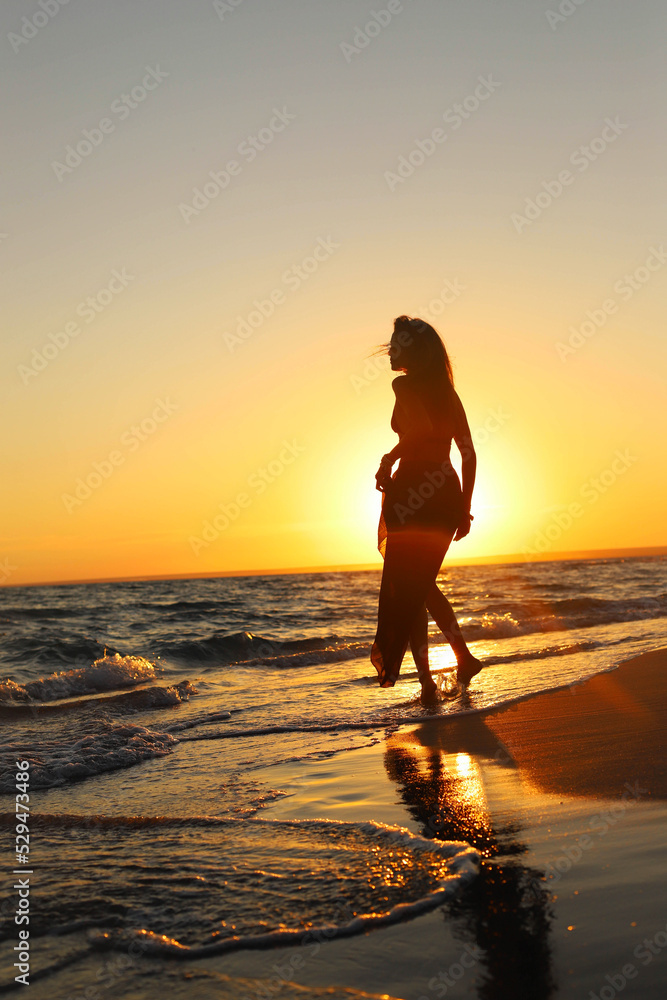 Young sexy girl on the beach at sunset in a swimsuit