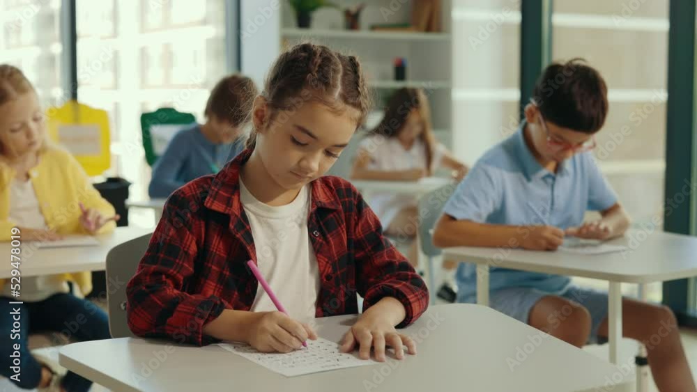 Exam in elementary school. Female beautiful pupil sits at a first desk in the classroom and fills out tests thinks about answers. Education children. Exam in elementary school. Female beautiful pupil sits at a first desk in the classroom and fills out tests thinks about answers. Education children.