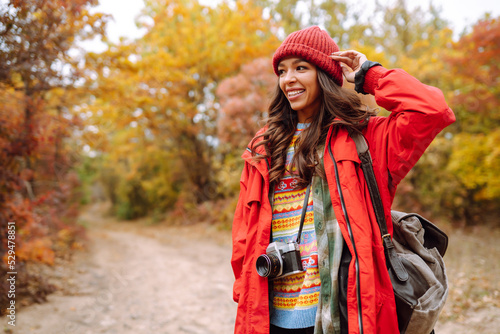 Beautiful woman taking pictures in the autumn forest. Smiling woman enjoying autumn weather. Rest, relaxation, lifestyle concept.