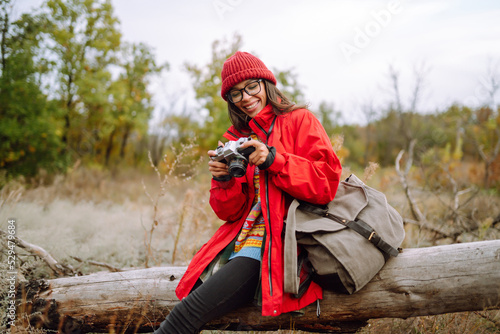 Beautiful woman taking pictures in the autumn forest. Smiling woman enjoying autumn weather. Rest, relaxation, lifestyle concept.