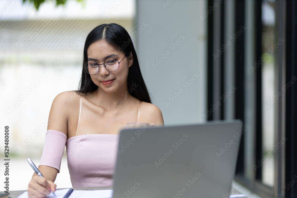 Charming and good-humored Asian woman is working on a laptop in the backyard. Working from home. Charming and good-humored Asian woman is working on a laptop in the backyard. Working from home.