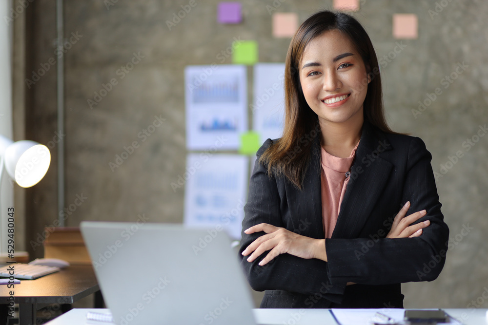 Portrait of a charming Asian businesswoman in the office looking at the camera while working on a computer laptop. Portrait of a charming Asian businesswoman in the office looking at the camera while working on a computer laptop.