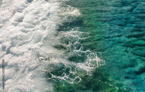 Beautiful natural texture of rolling sea waves surf with white foam and clear water with turquoise and green hues.