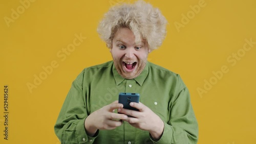 Wallpaper Mural Portrait of excited young man getting good news in smartphone message smiling texting using modern device on yellow color background Torontodigital.ca
