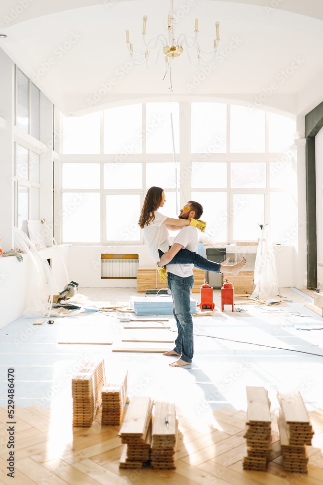 Happy newlyweds kissing and hugging are happy to move into a new house by taking out a mortgage. A couple in love make repairs together in an empty bright interior in a room in an indoor apartment. Happy newlyweds kissing and hugging are happy to move into a new house by taking out a mortgage. A couple in love make repairs together in an empty bright interior in a room in an indoor apartment.