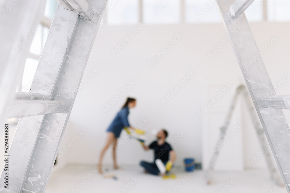 Young couple in love, the newlyweds are making repairs in an empty room, painting white walls, updating the house. A happy man and woman took out a mortgage and moved into a new house. Place for text 