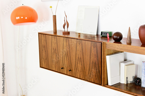 a vintage 60s mid century highboard sideboard made out of rosewood in denmark hanging on the wall in the living room danish design decorated furnished with expensive vases on top of it and books  photo